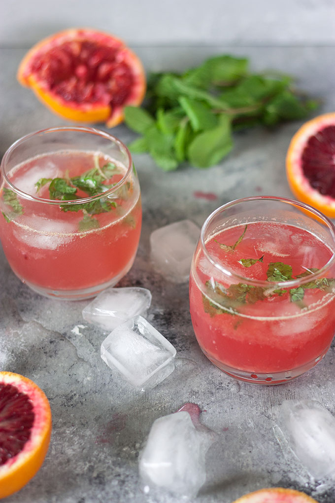 two blood orange cocktails on a grey board with cut winter citrus