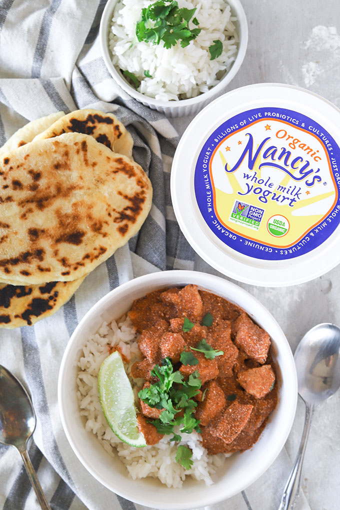 one bowl of chicken yogurt curry with naan on the left and a yogurt container