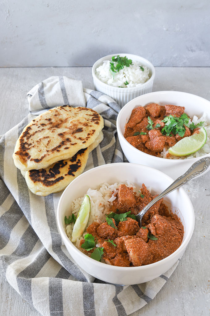 two bowls of curry, one bowl of rice and naan bread on a napkin