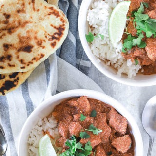 two bowls of chicken yogurt curry with naan bread on a napkin